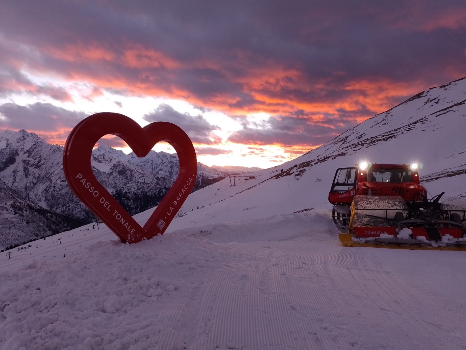 Cuore Passo del Tonale e La Baracca sulla neve al tramonto, con un gatto delle nevi accanto